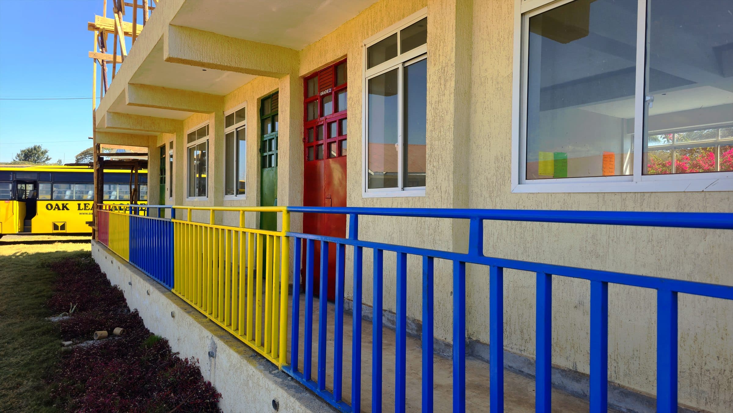 Colourful classroom doors and windows along the Oak Leaf Academy pre-primary block, with the school bus parked nearby.