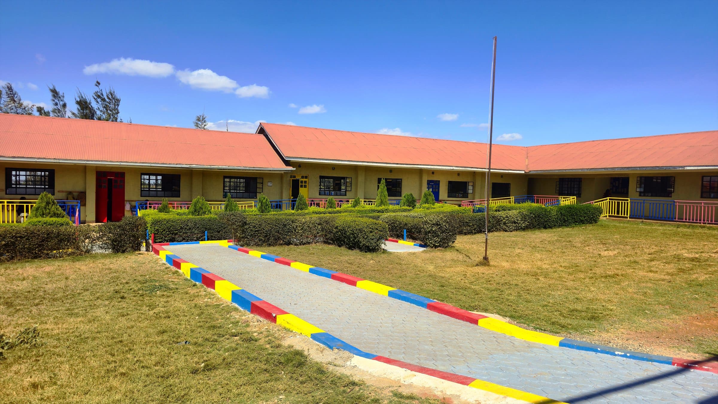 A paved, brightly kerbed walkway running the length of the Oak Leaf Academy classroom block, with lawns on either side.